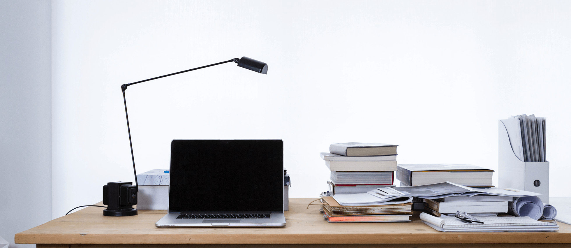 Ilustracja przedstawia laptop na biurku. Obok znajdują się lampka i książki.